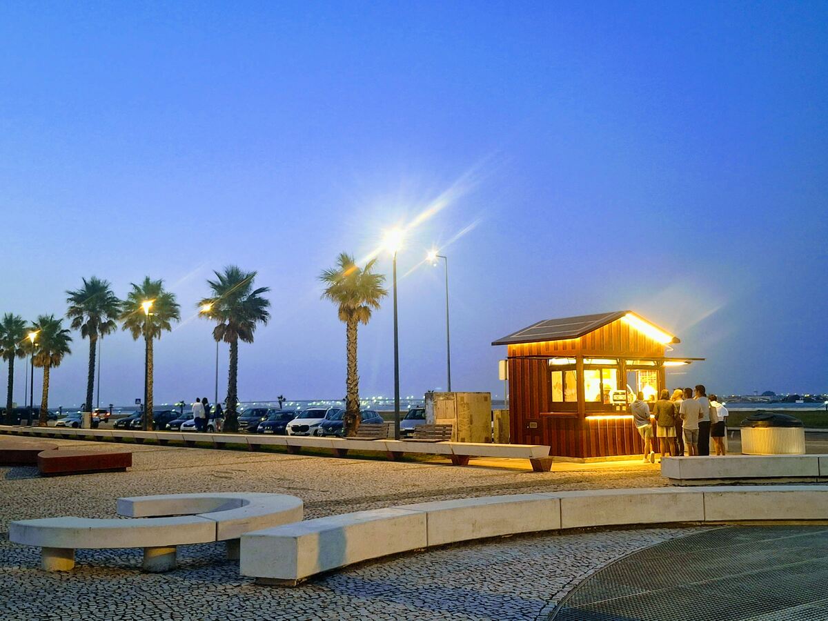 The photo shows a brightly lit kiosk on the lagoon promenade in Costa Nova, one of Aveiro's neighboring beach communities, at dawn.
