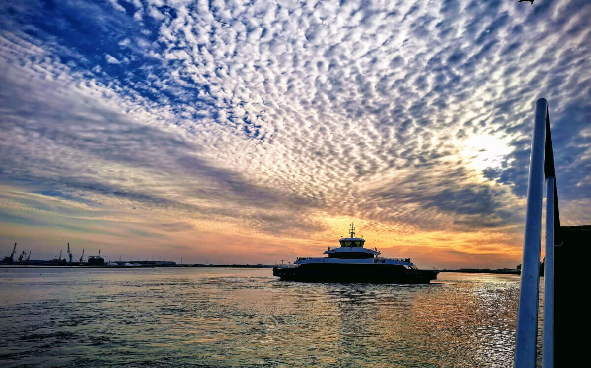 The image shows the São Jacinto electric ferry on its way to Forte da Barra during sunset.
